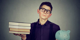 Boy with a stack of college books in one hand and a piggy bank in the other.