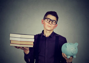 Boy with a stack of college books in one hand and a piggy bank in the other.