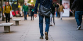 Rear view of a college student with a messenger bag walking to work.