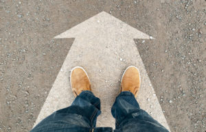 A person stands on an arrow to indicate choosing a path, like the guided pathways program helps students choose their career path.