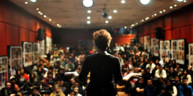 A woman in a public forum demonstrates TED Talks for higher education.