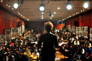 A woman in a public forum demonstrates TED Talks for higher education.