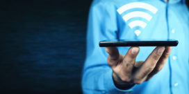 A man holds a device with a campus wi-fi symbol above it.