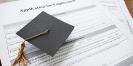 This graduation cap on top of a job application illustrates the path of recent graduate pursuing career goals.