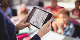 A teacher can teach with tech more effectively when learning how to use it right, like this teacher holding a tablet teaching in the classroom.